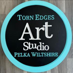 photo of Torn Edges Art Studio business. Round with black background and blue border.