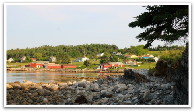 Colourful wooden houses on a hill facing the sea taken from a shaded rock beach.