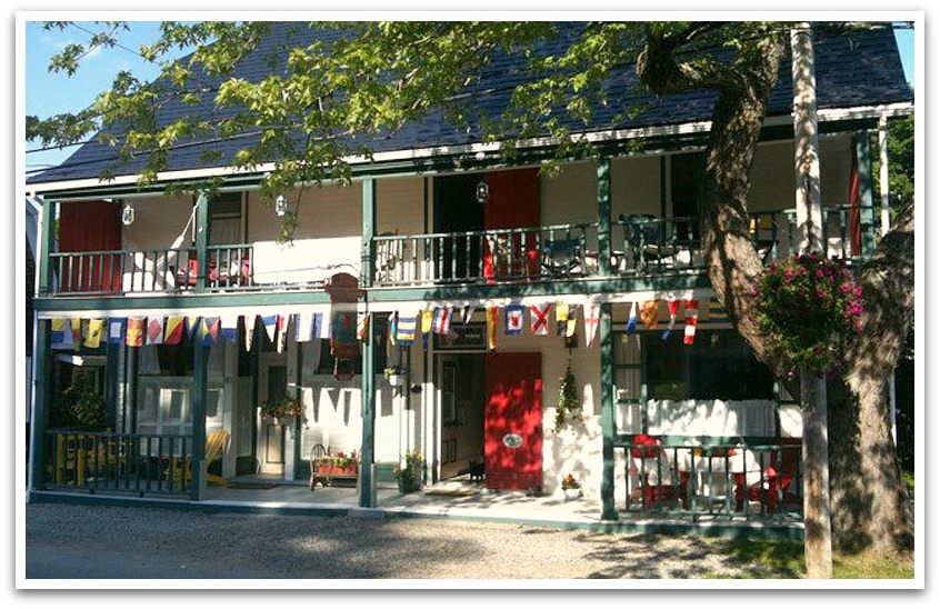 White building with green framing and red doors with sailing flags hanging from the balcony.