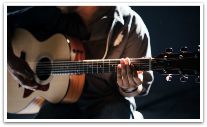 Man Playing an acoustic guitar in dim light.